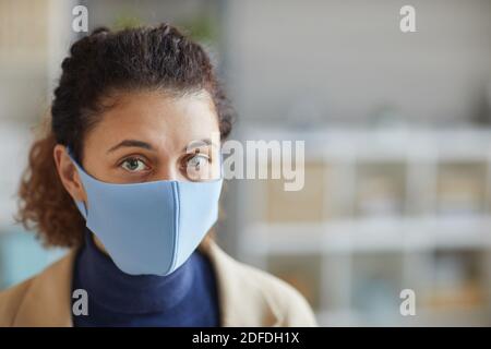 Gros plan d'une jeune femme dans un masque de protection regardant l'appareil photo au bureau Banque D'Images