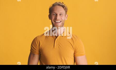 Jeune homme barbu souriant vêtu d'une tenue décontractée qui a l'air heureux sur l'appareil photo sur un arrière-plan coloré Banque D'Images