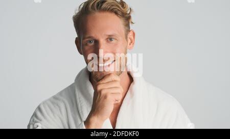 Beau sourire barbu homme en peignoir de regarder heureux sur l'appareil photo isolé sur fond blanc Banque D'Images