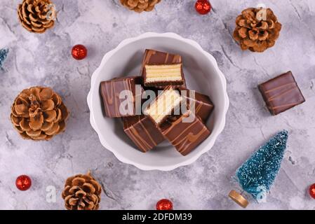 Pralines de gâteau d'hiver allemandes superposées appelées 'Baumkuchen' émaillées de chocolat dans un bol, entouré par la décoration de Noël de saison Banque D'Images