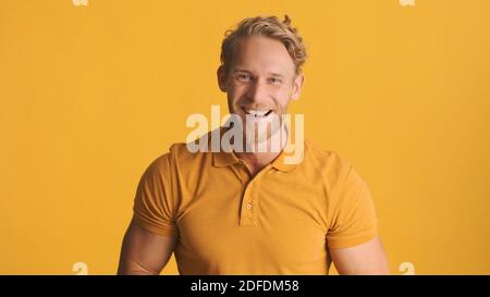 Jeune homme barbu attrayant se réjouissant de l'appareil photo sur fond jaune. Expression joyeuse Banque D'Images