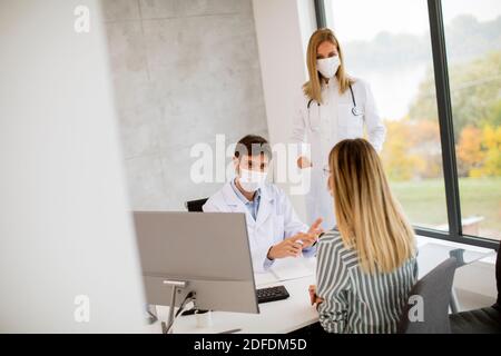 Couple médical médecins avec masques médicaux de protection du visage parler avec jeune femme et l'utilisation de l'ordinateur dans l'offic Banque D'Images