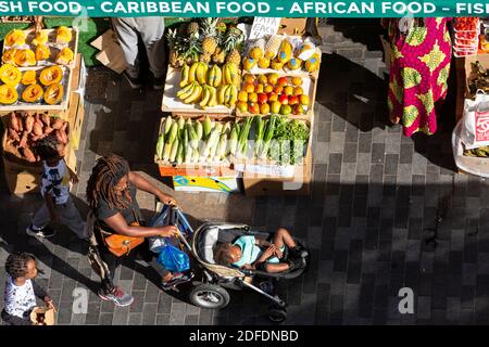 Une femme avec poussette passant devant un stand de rue à Brixton Market, Electric Avenue, Brixton, Londres Banque D'Images