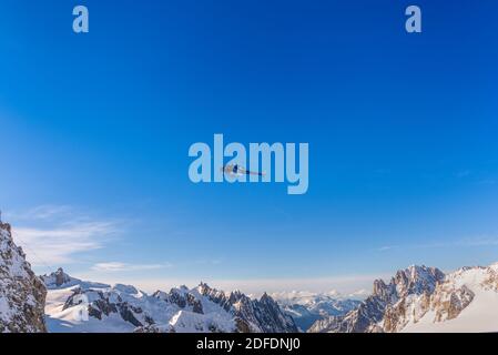 Hélicoptère bleu en vol au-dessus des sommets enneigés des montagnes un jour clair contre le ciel bleu Banque D'Images