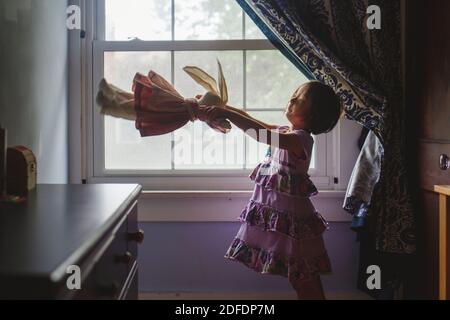 Une petite fille mignonne tient par fenêtre jouant avec un animal doux farci Banque D'Images