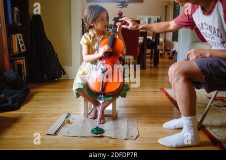 Un père se penche pour aider une petite fille à pratiquer jouer un violoncelle Banque D'Images