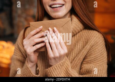 Vue rapprochée d'une jeune femme souriante à tête rouge tenant dans les mains une enveloppe en papier devant elle. Banque D'Images