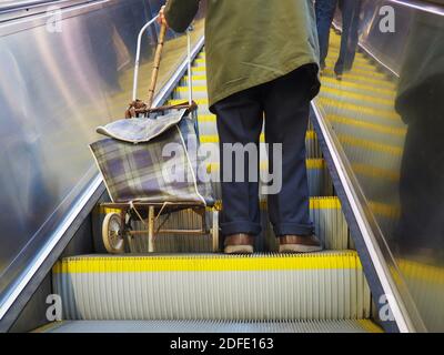 Vieux pauvre retraité retraité homme debout avec un chariot et bâton sur l'escalier roulant de métro à Budapest, Hongrie Banque D'Images