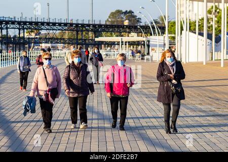 Huelva, Espagne - 3 décembre 2020: Personnes marchant sur la promenade de Huelva au coucher du soleil, portant des masques protecteurs ou médicaux pendant l'état d'alarme et qu Banque D'Images