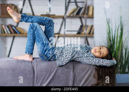 Jeune adolescente calme avec de longs cheveux, allongé sur le dos sur un canapé confortable, les mains détendues derrière sa tête Banque D'Images