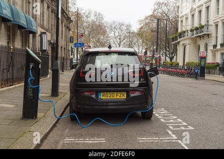 Une BMW i3 électrique se recharge dans une petite rue avec un câble d'alimentation bleu qui mène à un boîtier de chargement. Londres Banque D'Images