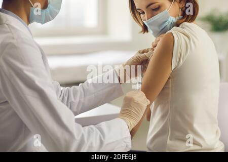 Jeune femme dans le masque de visage recevoir Covid-19 ou antiviral de grippe vaccin au cabinet du médecin Banque D'Images