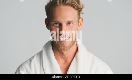 Beau homme confiant barbu en peignoir heureux regardant dans l'appareil photo et souriant isolé sur fond blanc Banque D'Images