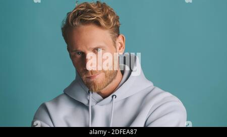 Beau gars élégant en sweat à capuche isolé sur fond coloré. Modèle masculin posé en studio avec confiance Banque D'Images