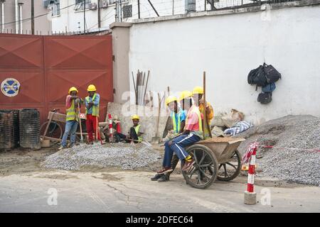 Antananarivo, Madagascar - 24 avril 2019: Groupe d'ouvriers malgaches inconnus en casques et vestes haute visibilité, se reposant sur le chantier, assis et Banque D'Images