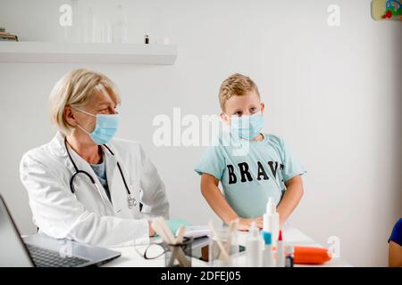 Médecin souriant parlant avec un garçon. Ils portent un masque de protection. Banque D'Images