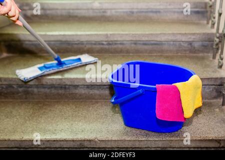 Équipement de nettoyage, un seau en plastique bleu avec un chiffon en microfibre jaune et rose, debout sur des escaliers en granit gris. Une vadrouille à main pour essuyer l'escalier Banque D'Images