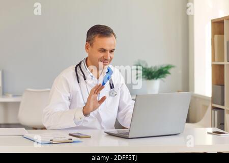 Homme souriant médecin assis et saluant le patient avec la main en ligne sur ordinateur portable Banque D'Images