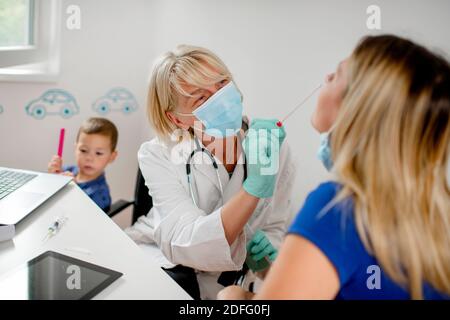 Médecin prenant un échantillon du nez d'une jeune femme à l'aide d'un coton-tige. Ils portent un masque facial. Banque D'Images