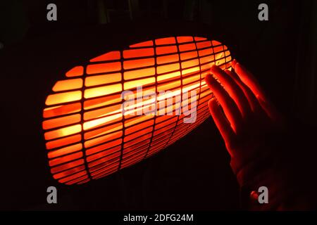 Le chauffage infrarouge réchauffe les mains dans l'obscurité Banque D'Images