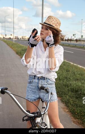 Fun brunette young woman cyclist applique les cosmétiques le road Banque D'Images