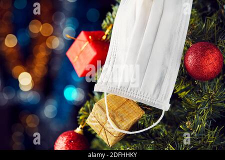 Masque médical suspendu sur un arbre de Noël avec des ornements et des lumières de bokeh arrière-plan. Fête de Noël en toute sécurité pendant le Covid-19 Banque D'Images