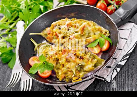 Aubergine farcie au fromage fumé, tomates, oignons, carottes à l'ail, fromage et herbes dans une casserole sur une serviette en bois noir Banque D'Images