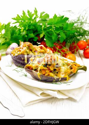 Aubergine farcie au fromage fumé, tomates, oignons, carottes à l'ail, fromage et herbes dans une assiette ovale sur une serviette en bois Banque D'Images