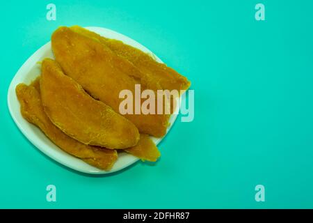 Morceaux de mangue séchée sur une assiette blanche. Plaque blanche isolée sur fond bleu. Desserts sucreries pour cafétérias, bars, petits restaurants. Banque D'Images