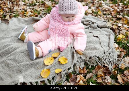 Belle petite fille assise sur le tissu écossais. Enfants à l'extérieur. Adorable petite fille en vêtements chauds au pique-nique dans le parc d'automne le jour ensoleillé. Banque D'Images