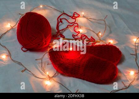 Chaussettes de noël en laine de couleur rouge faites à la main, aiguille en crochet et boule en laine illuminée de lumières de noël miniatures. Arrière-plan de l'espace de copie. Fa d'hiver Banque D'Images