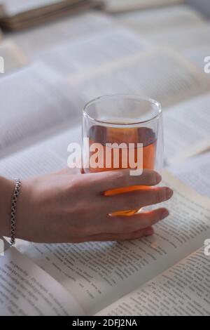 Une main avec un bracelet argenté tenant une tasse de thé avec un double fond sur les pages de livres - vertical photo Banque D'Images