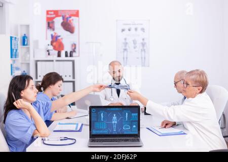 Le médecin Matude donne une radiographie à une jeune infirmière pendant la réunion du personnel dans la salle de conférence. Thérapeute expert en clinique parlant avec des collègues de la maladie, professionnel de la médecine. Banque D'Images