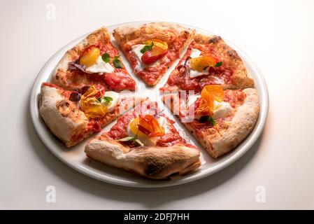 Pizza gourmande, réinterprétation appétissante de la pizza de Naples classique avec tomate, mozzarella, basilic et peau de poivre croquante. Six tranches sur la pl Banque D'Images