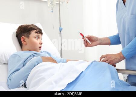 Peur enfant allongé dans le lit dans la chambre d'hôpital effrayé par l'aiguille de l'infirmière de la seringue effectue un test sanguin Banque D'Images