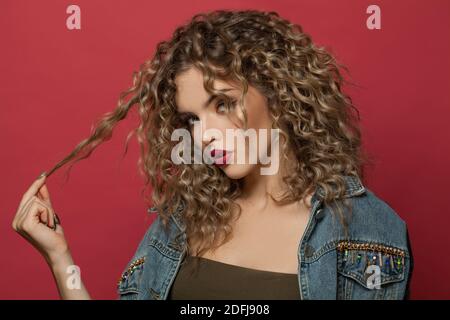 Belle femme avec des cheveux bouclés posé sur fond rouge Banque D'Images
