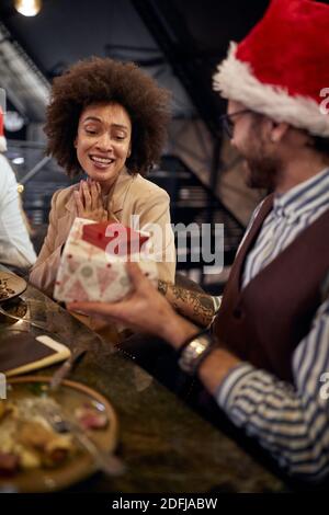 Un employé qui donne un cadeau du nouvel an à une collègue lors d'un dîner d'entreprise dans un restaurant dans une atmosphère de vacances. Ensemble, nouvel an, célébration Banque D'Images