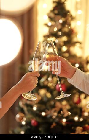 Mains de jeune couple joyeux se clinquant avec des flûtes de champagne Tout en toaster pour Noël lors de la célébration contre le sapin décoré Banque D'Images