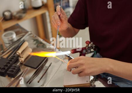 Mains de jeunes femmes artisanales contemporaines assis sur le lieu de travail et brûler la pièce au feu tout en la tenant par-dessus le brûleur atelier Banque D'Images