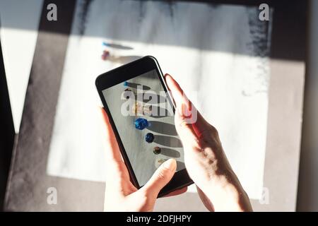 Mains de jeunes femmes avec smartphone prendre des photos de perles de verre de différentes tailles, formes et couleurs sur une table en bois peinte en blanc Banque D'Images