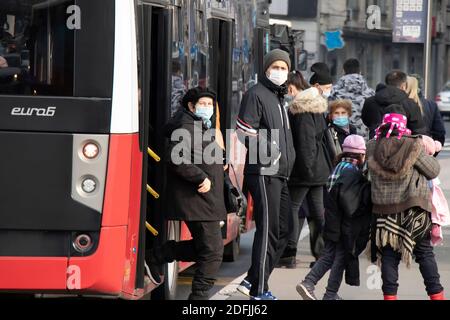 Belgrade, Serbie - 2 décembre 2020 : personnes portant un masque chirurgical tout en prenant un bus public à l'arrêt d'un bus de ville , en hiver Banque D'Images