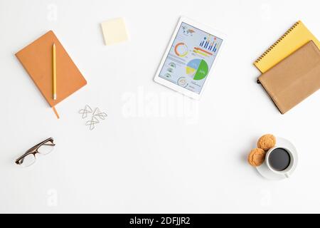 Vue de dessus des fournitures de bureau ou de courtier, y compris des carnets, une tablette, des lunettes, du papier à lettres, un crayon, une tasse de café avec des biscuits et des clips Banque D'Images