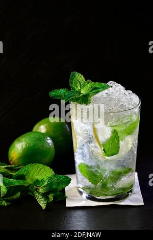 Gros plan d'un cocktail froid de mojito avec des feuilles de menthe et des cimes hors foyer à l'arrière sur fond sombre. Alcool et loisirs. Banque D'Images