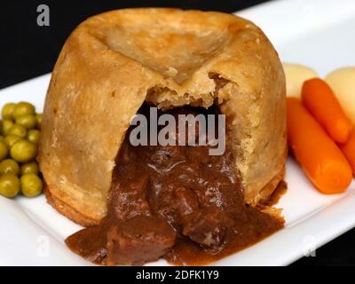 Cuire à la vapeur le steak et le pudding aux reins sur une assiette blanche avec des petits pois et des carottes et de la sauce sur l'assiette. Banque D'Images