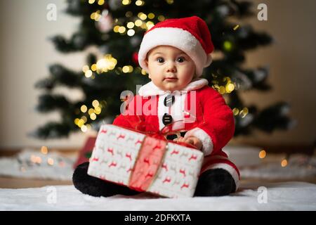 adorable petit garçon en costume de père noël une fausse fourrure douce devant un arbre de noël Banque D'Images