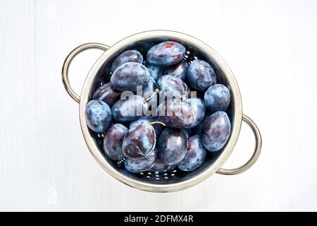 Prunes pourpres dans une passoire sur une table en bois blanc.Vue de dessus, espace de copie Banque D'Images