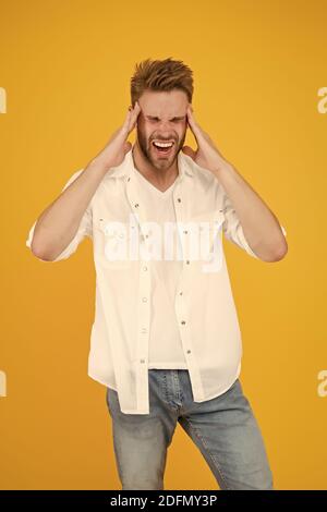 Migraine de tête et spasme. Problèmes de santé. Vie d'affaires. Mal de tête horrible. Bel homme dans un Jean chemise souffrant de douleur de tête. Homme fatigué et stressant fond jaune. Concept de vie stressante. Banque D'Images