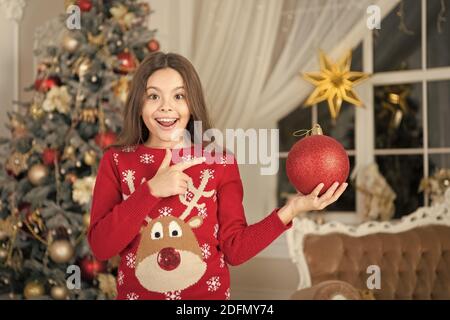 Le rouge est mon préféré. Décor d'attributs de Noël. Petite fille près de l'arbre de Noël. Enfant célébrer Noël à la maison. Traditions d'hiver. Adorable gamin excité porter le chandail de noël. Boutique cadeaux concept. Banque D'Images