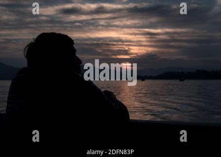 Silhouette d'un homme regardant le coucher du soleil sur un lac Banque D'Images
