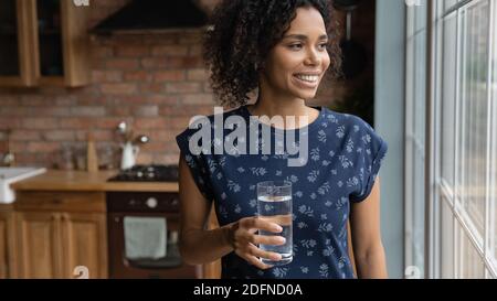 Jeune femme afro-américaine rêveuse tenant un verre d'eau. Banque D'Images